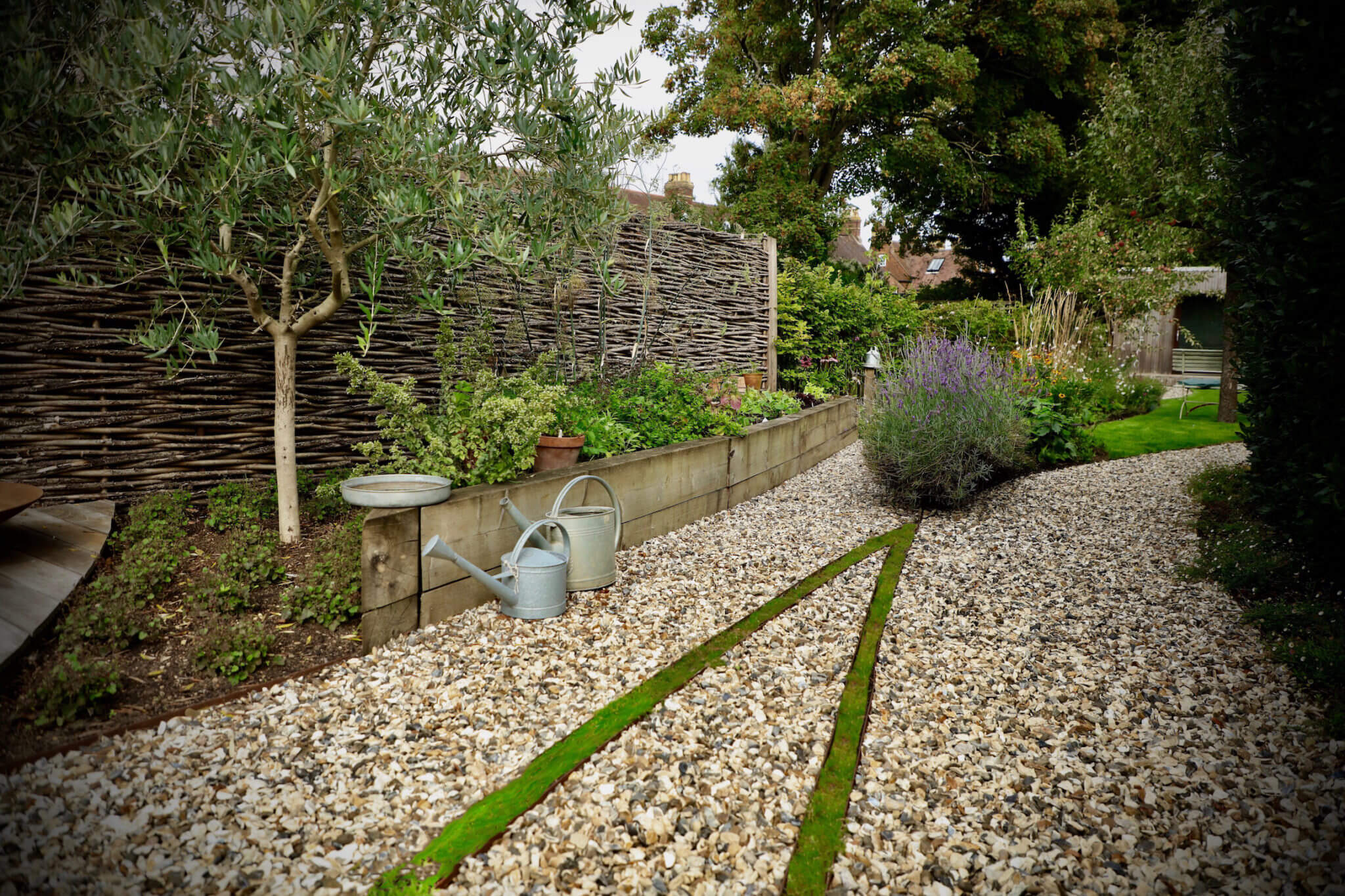 A raised bed filled with vegetable plants and two metal watering cans next to it