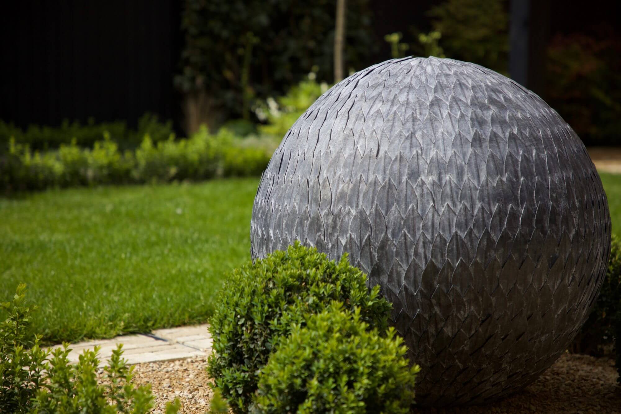 Spherical garden sculpture next to topiary and lawn