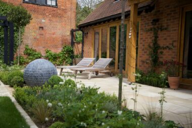 Two wooden sun loungers in front of french windows with a flower bed