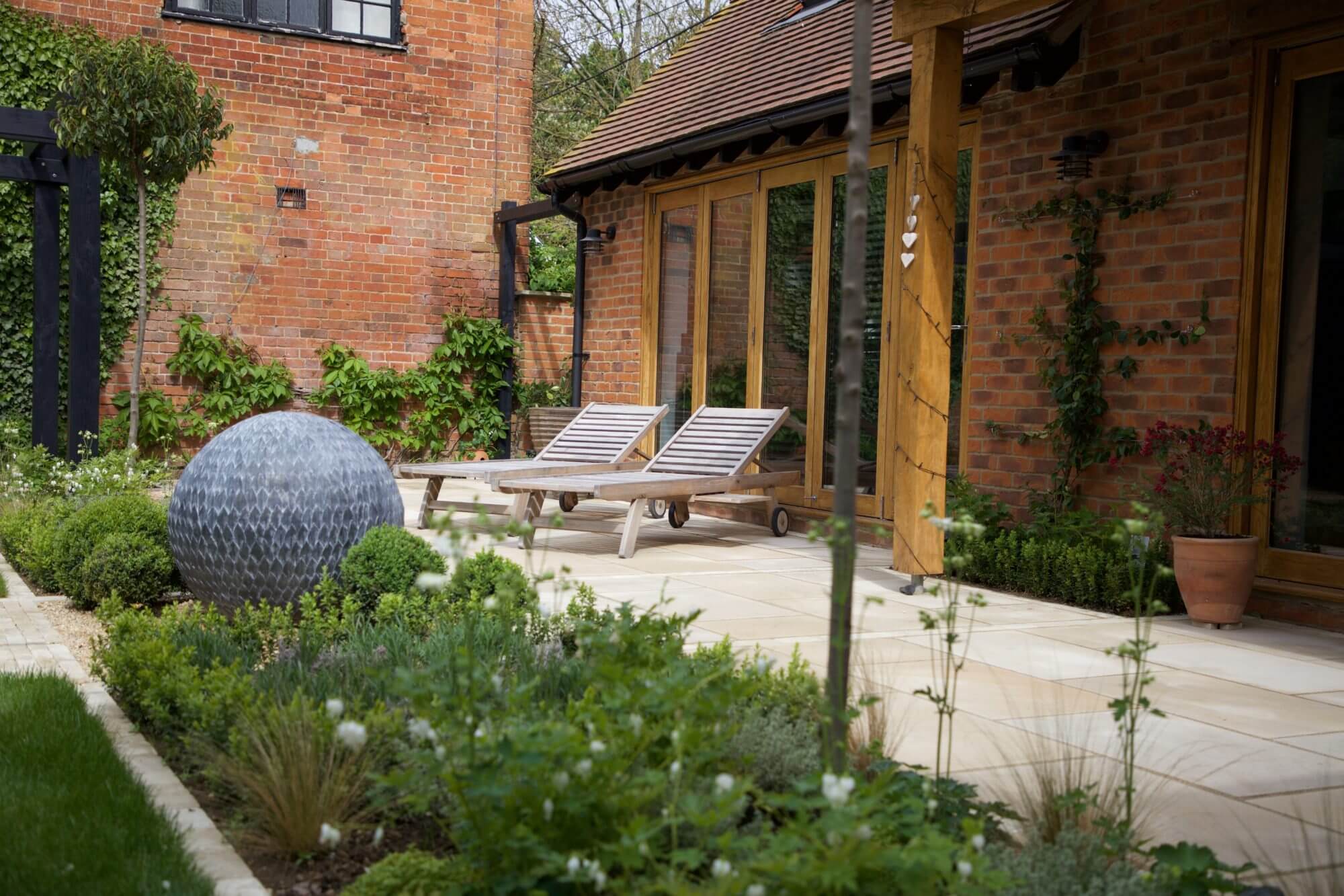 Two wooden sun loungers in front of french windows with a flower bed