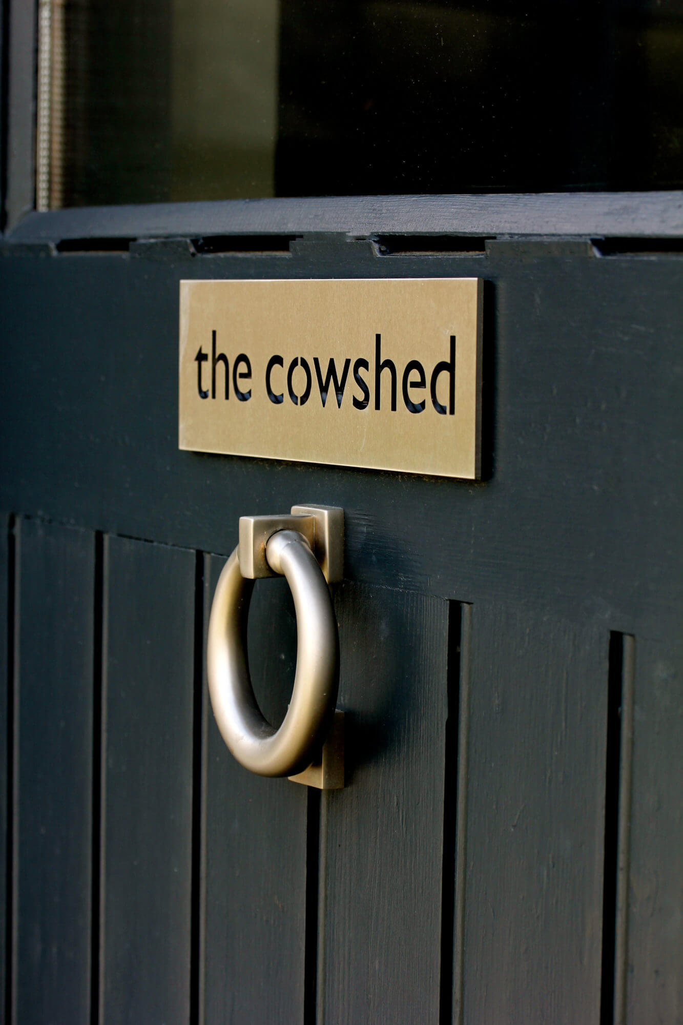 a blue barn conversion front door with knocker and sign saying the cowshed