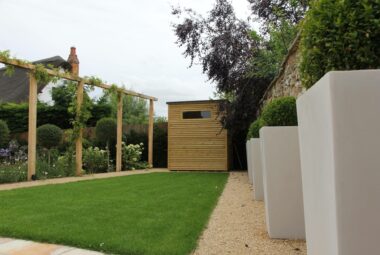 Cube planters with topiary balls inside of them and pergola with climbing plants