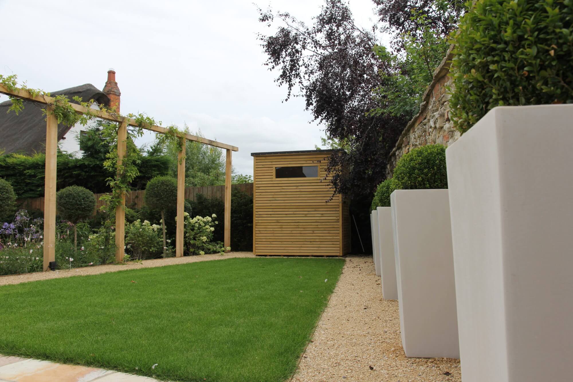 Cube planters with topiary balls inside of them and pergola with climbing plants