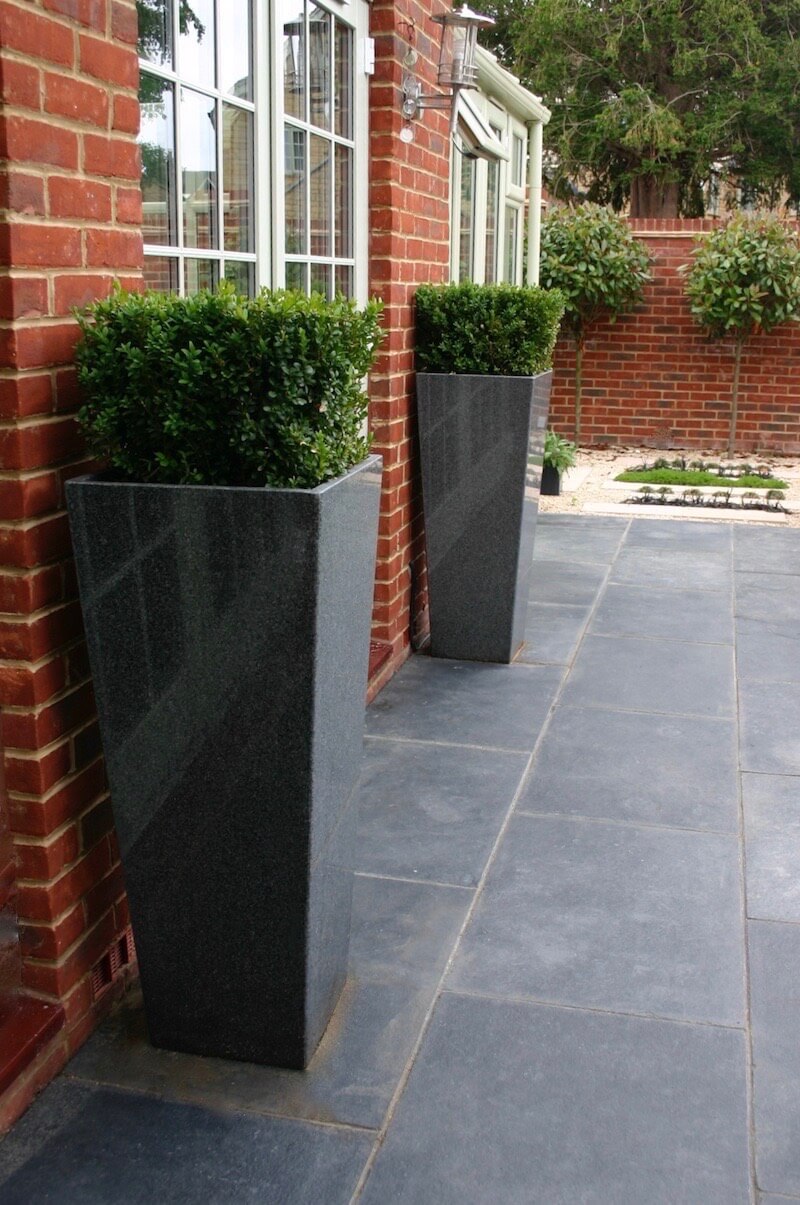 Cube topiary in grey granite planters against red brick wall