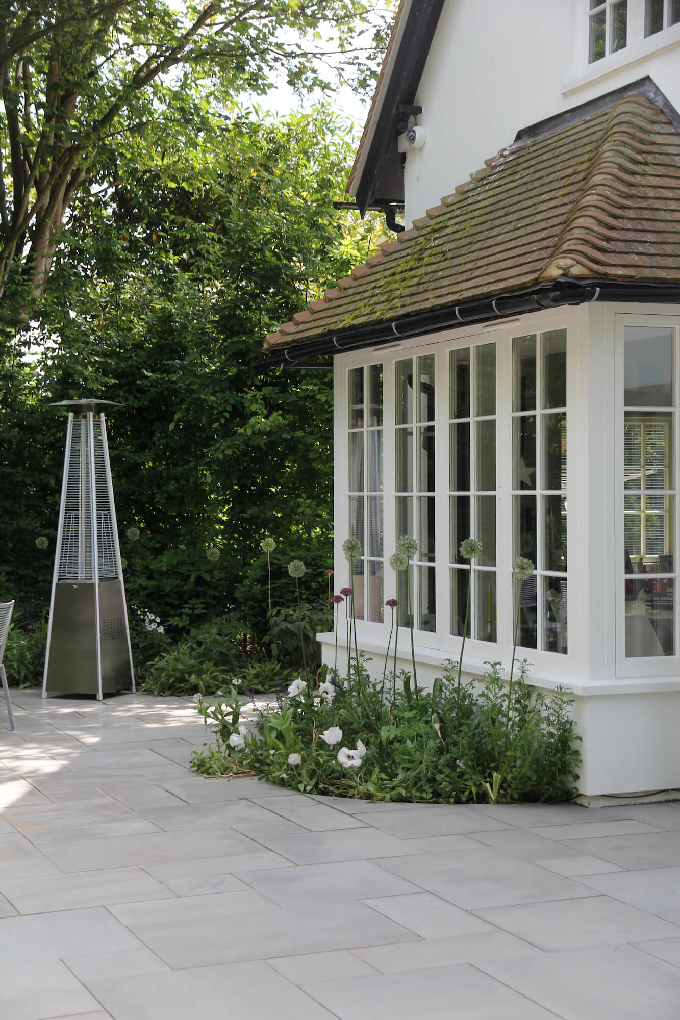 White alliums in front of big bay windows on patio with an outdoor heater