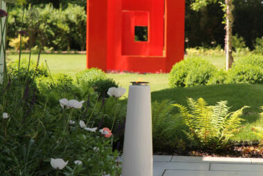 Giant contemporary red square sculpture sitting in the middle of a lawn