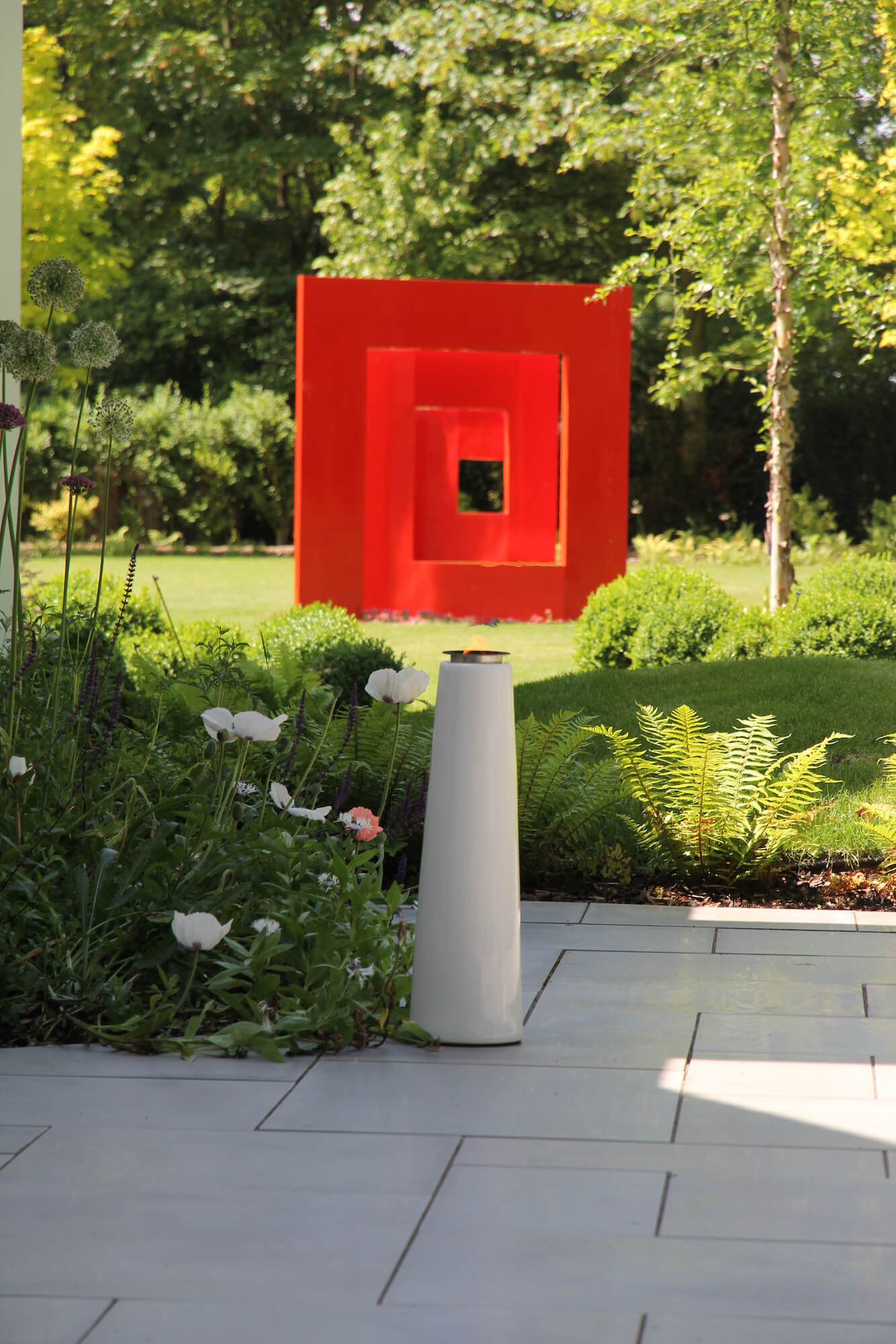 Giant contemporary red square sculpture sitting in the middle of a lawn