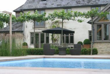Cotswolds garden with swimming pool, farmhouse and manicured planting