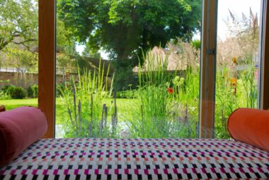 Colourful couch in front of french doors. Through the doors is a meadow of flowers