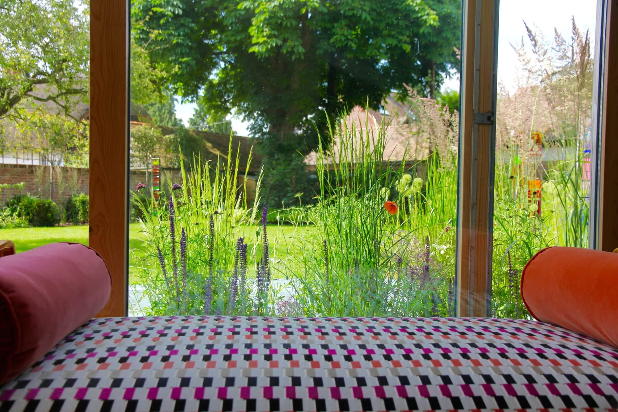 Colourful couch in front of french doors. Through the doors is a meadow of flowers