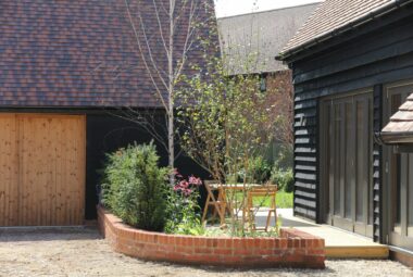 Red brick corner wall with trees next to wooden cladded house