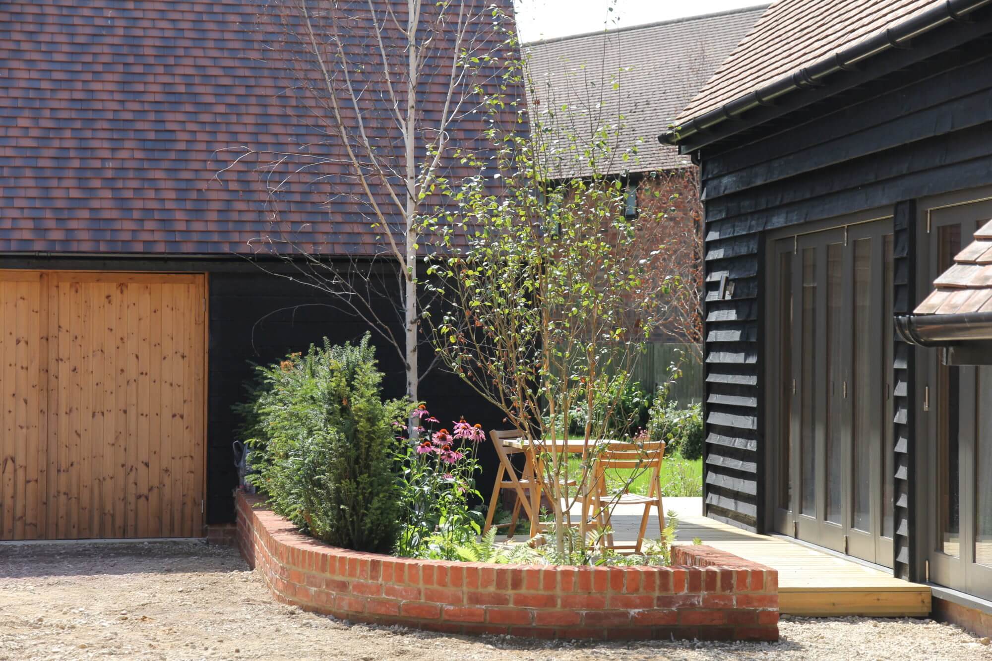 Red brick corner wall with trees next to wooden cladded house