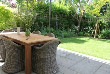 Wrap around wicker tub chairs at a table in the garden. There are freshly picked flower on the table