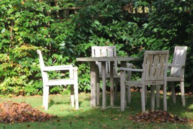 Wooden table and chairs in garden with pile of autumn leaves