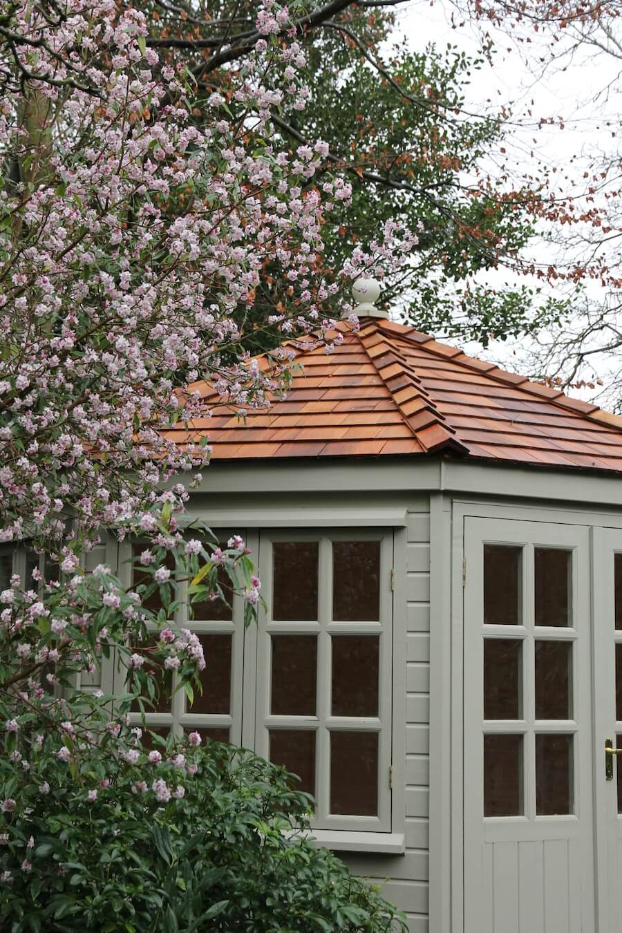 private garden summer house behind pink blossom tree