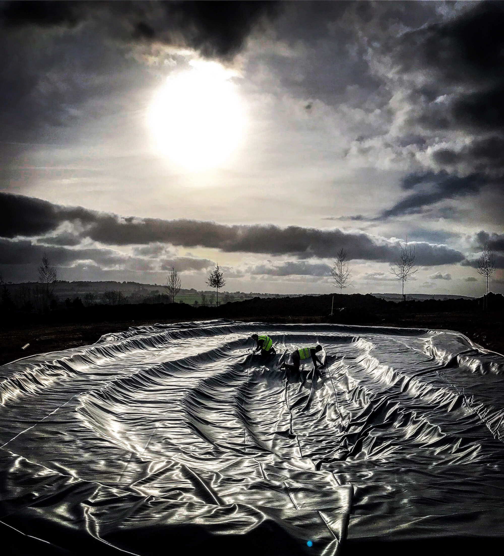 a massive wildlife pond under construction with it's rubber liner being laid by HC Landscapers in sunset