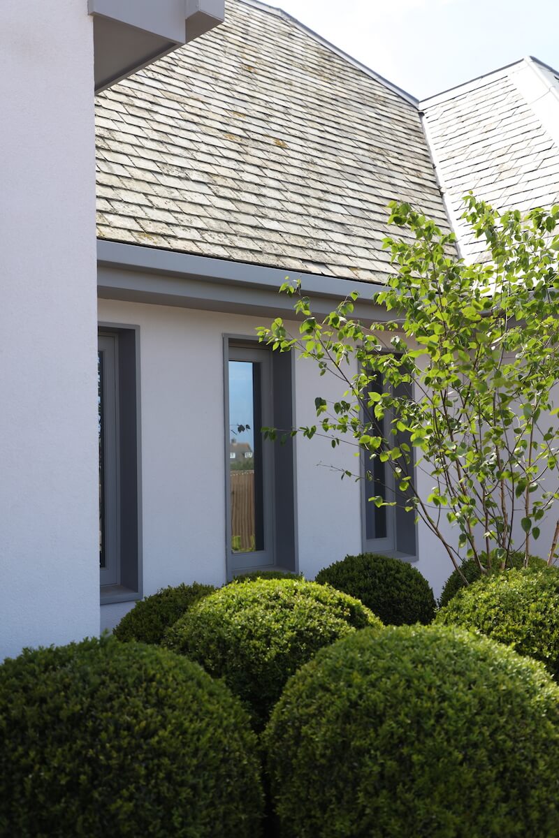 a Cornwall house painted white with grey windows and green topiary plants