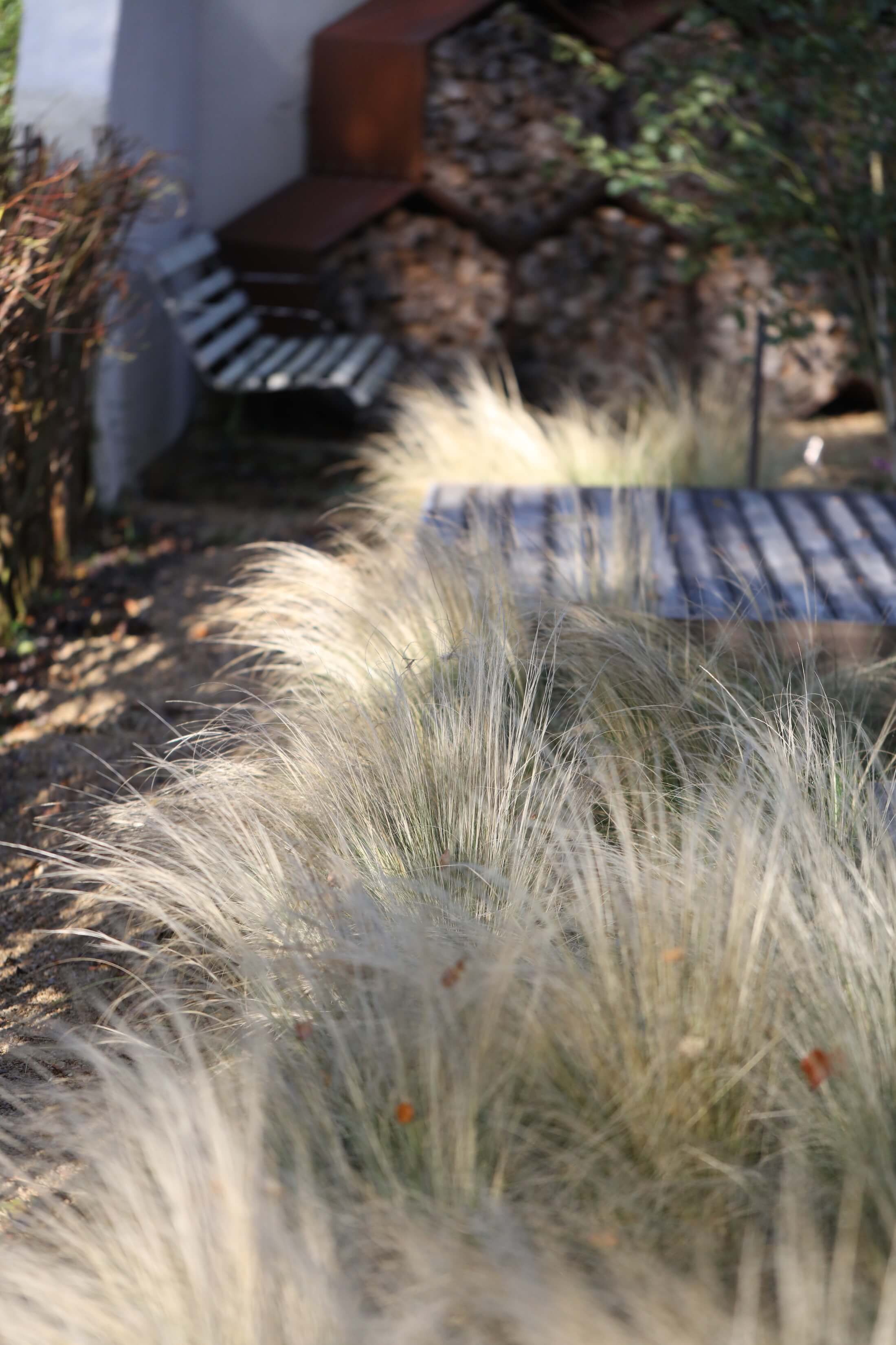 autumn garden with grasses and deck, hexagon log stores and wood bench