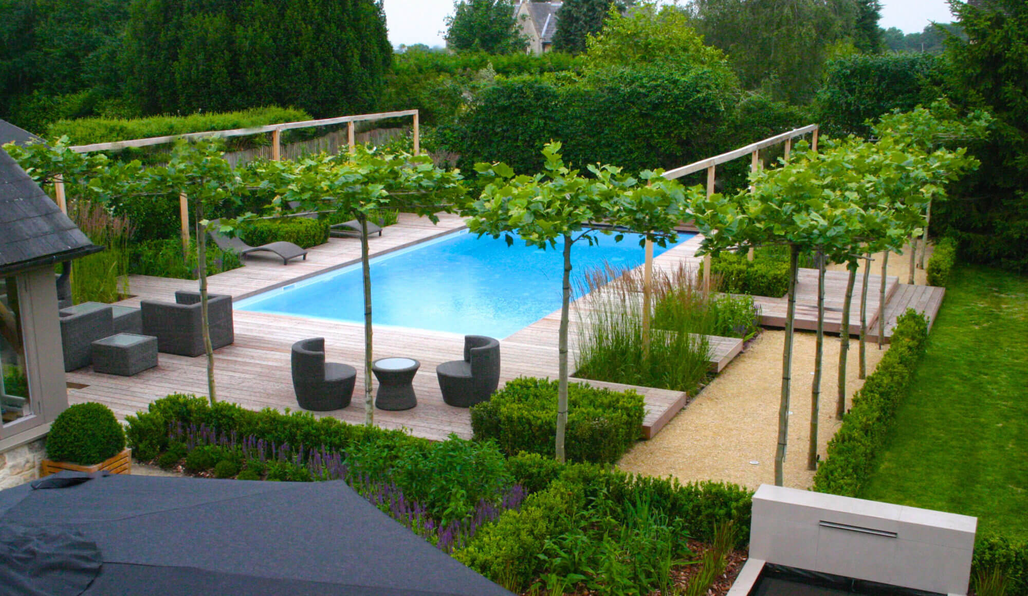 a modern swimming pool bright blue water surrounded by deck and flowers in the Cotswolds by garden designers