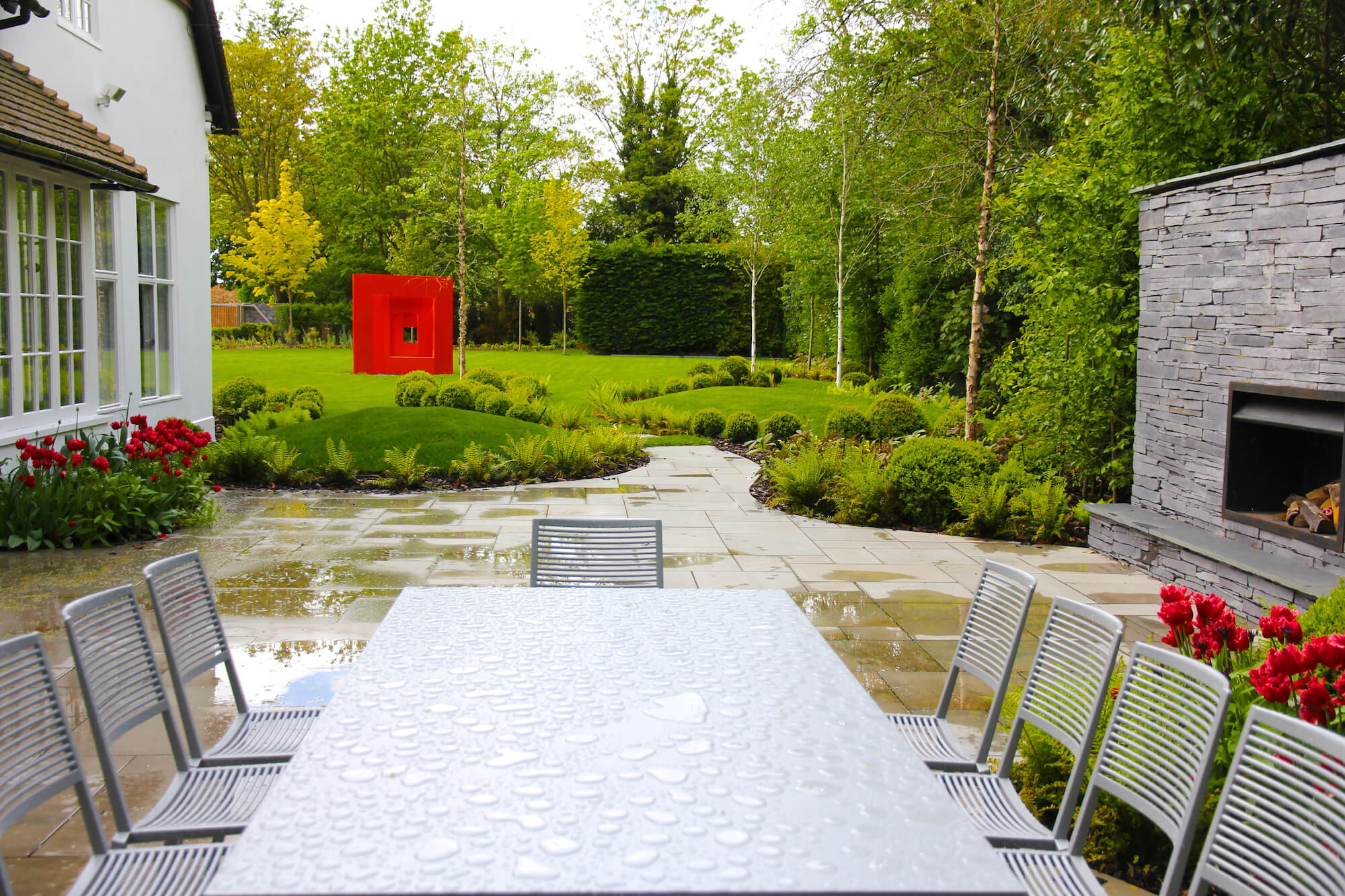 Metal outdoor table and chairs after a rain shower with red tulips in the background