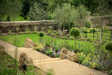 Hoggin pathway and steps with borders of wild flower meadow and trees with estate fencing