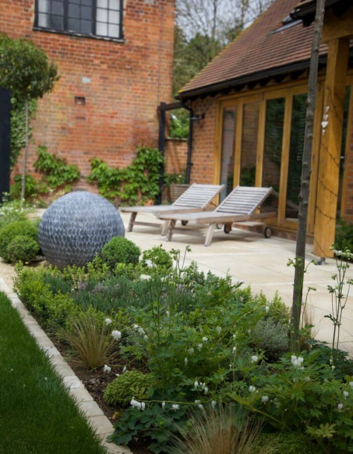 Chair loungers and sphere sculpture with green planting installed next to garden building