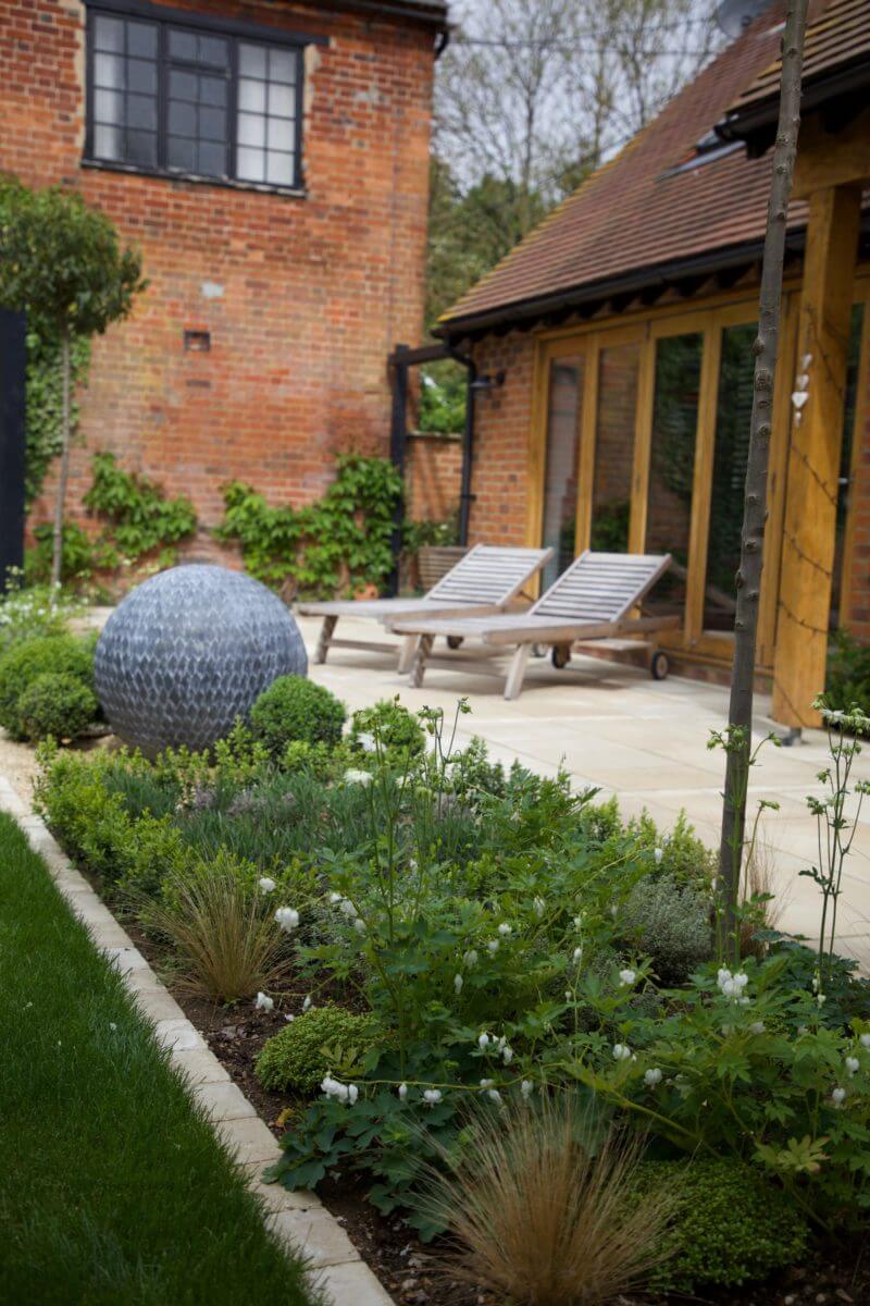 Chair loungers and sphere sculpture with green planting installed next to garden building
