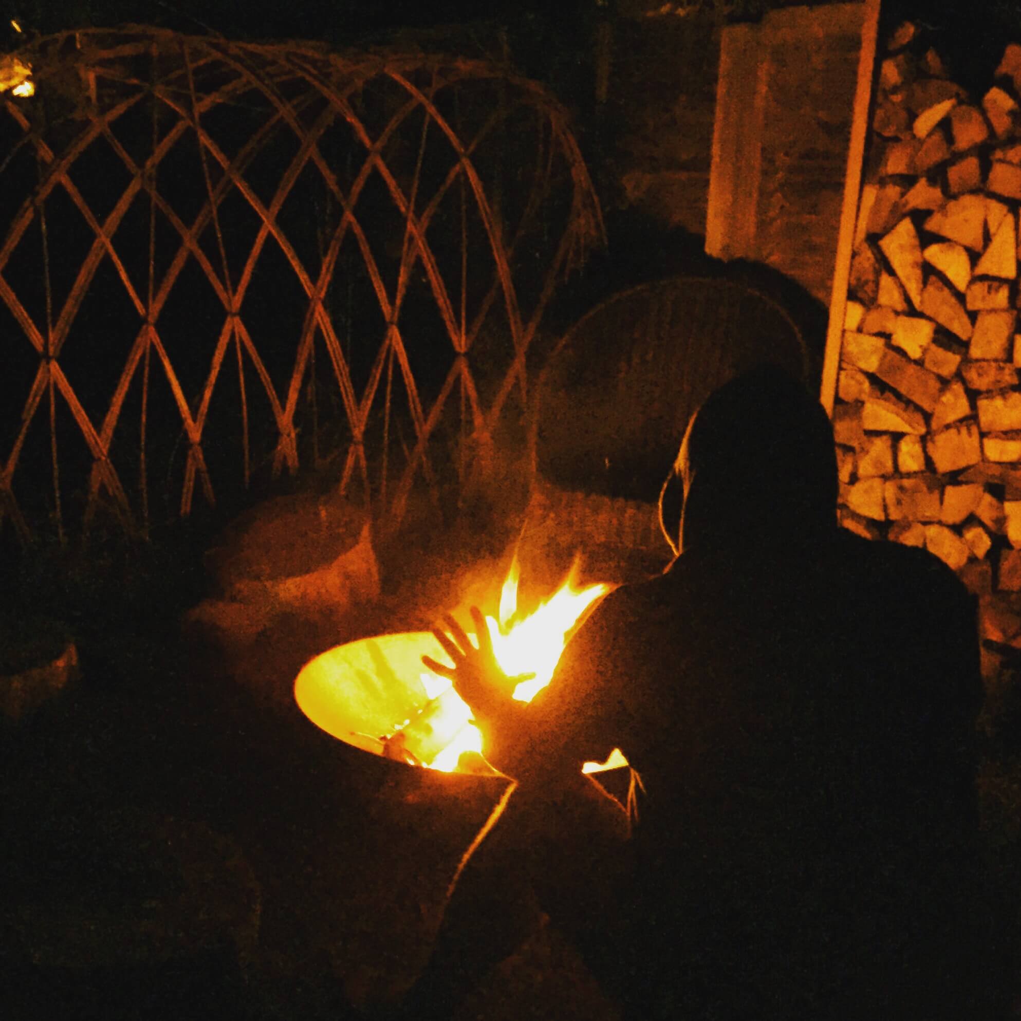 hooded figure outdoor in autumn in front of a fire pit with woven willow fencing