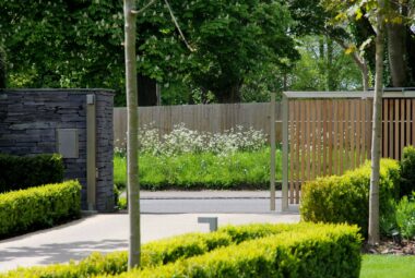 Automatic bespoke gates partially open with wild flowers on the grass verge opposite