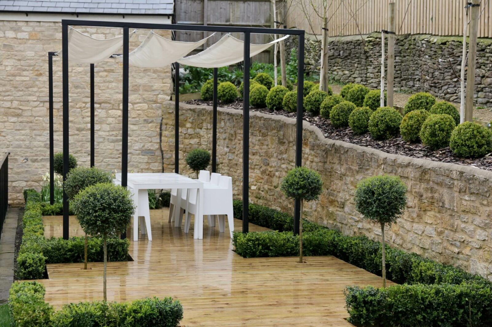 black metal pergola with weather sail over white table and chairs