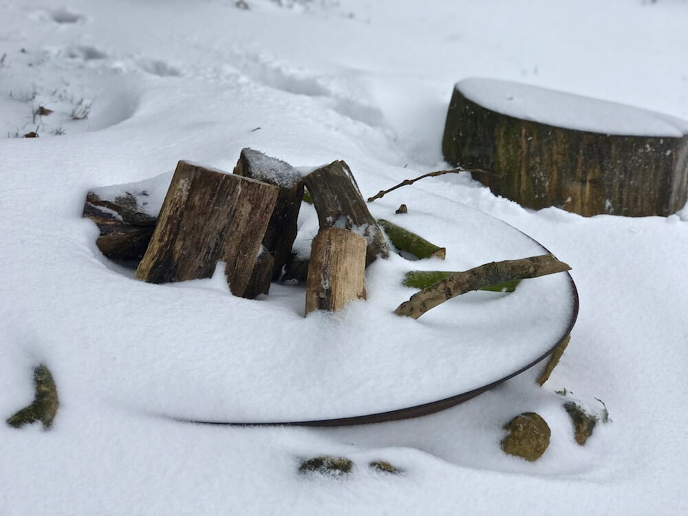 a fire pit with logs filled with snow in a cotswolds landscape