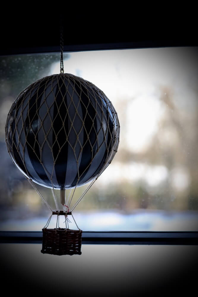Childs mobile of an air balloon in front of a window with a cotswolds landscape behind