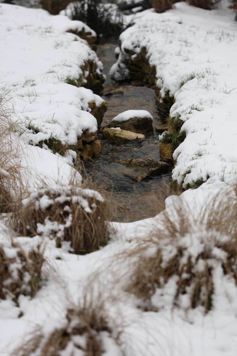 a stone rill breaks through snow in a cotswolds landscape design