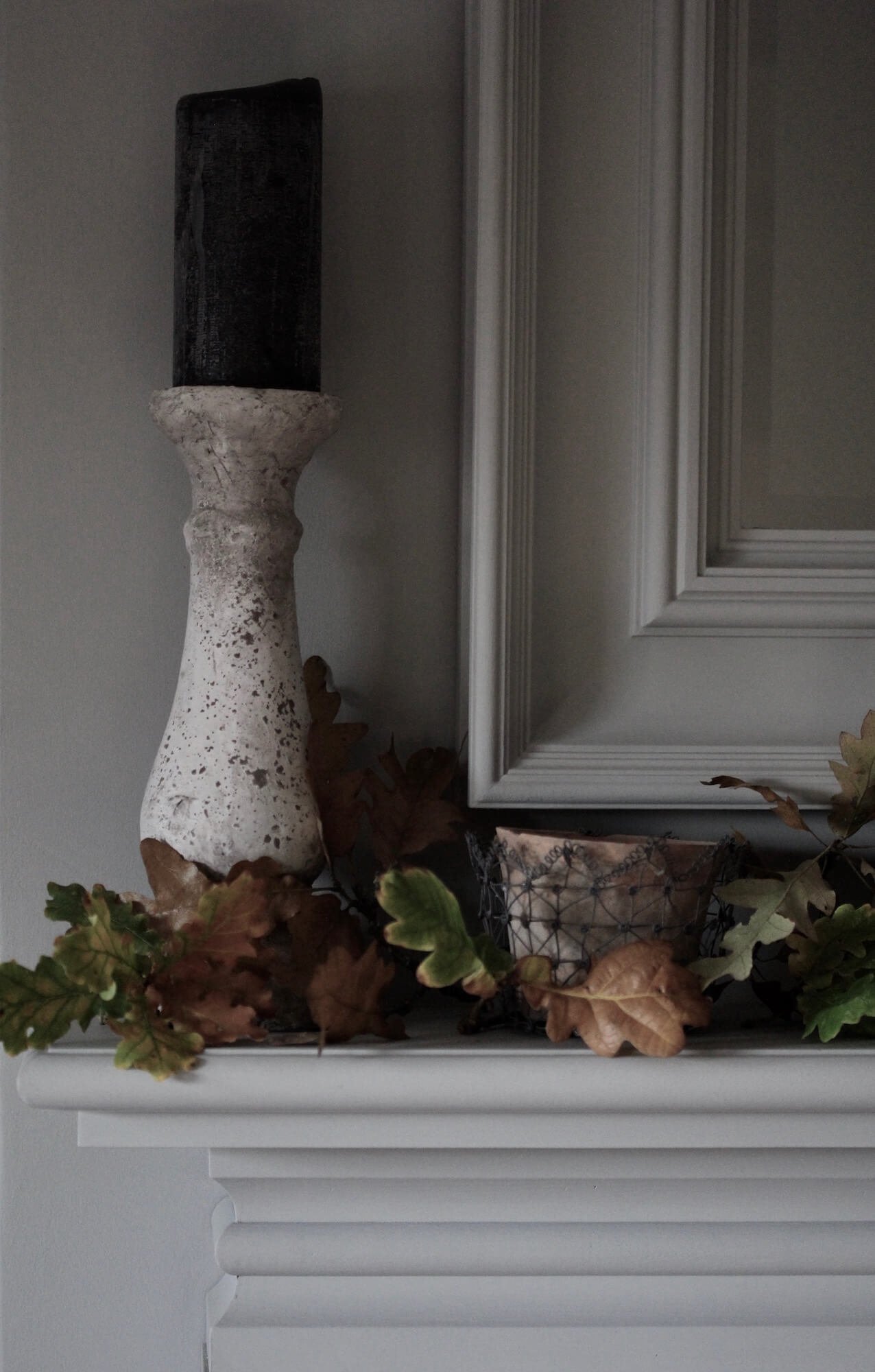 a mantlepiece painted in Farrow & Ball paint with Autumn leaves arranged around a stone candlestick and blue candle