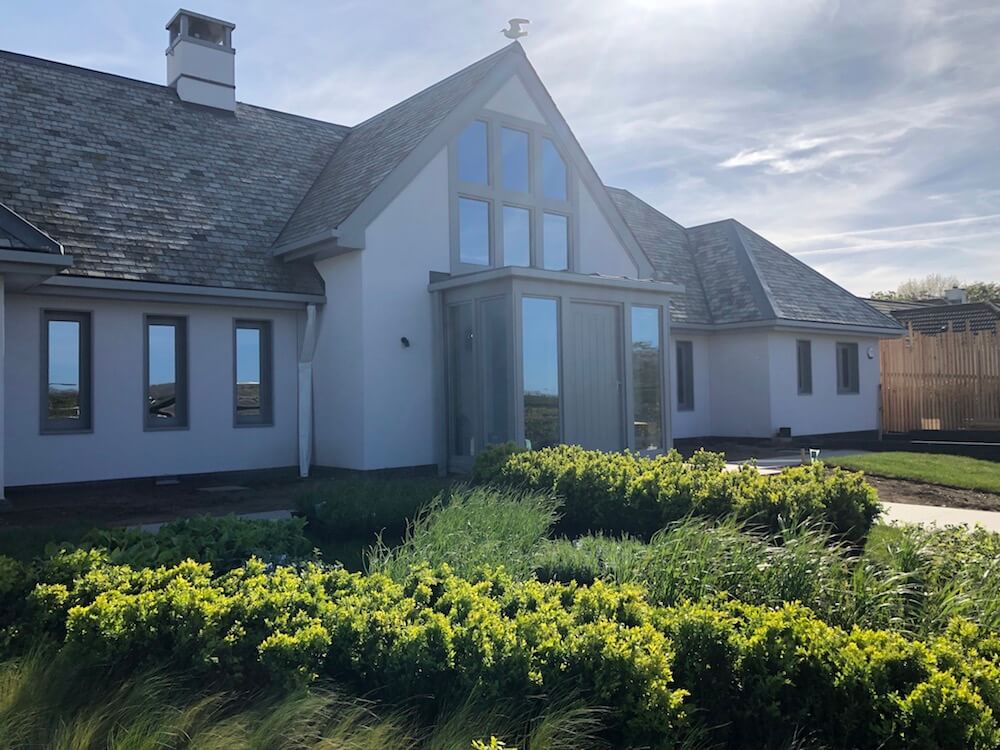 white and grey Cornwall house with green landscaping and seagull on roof