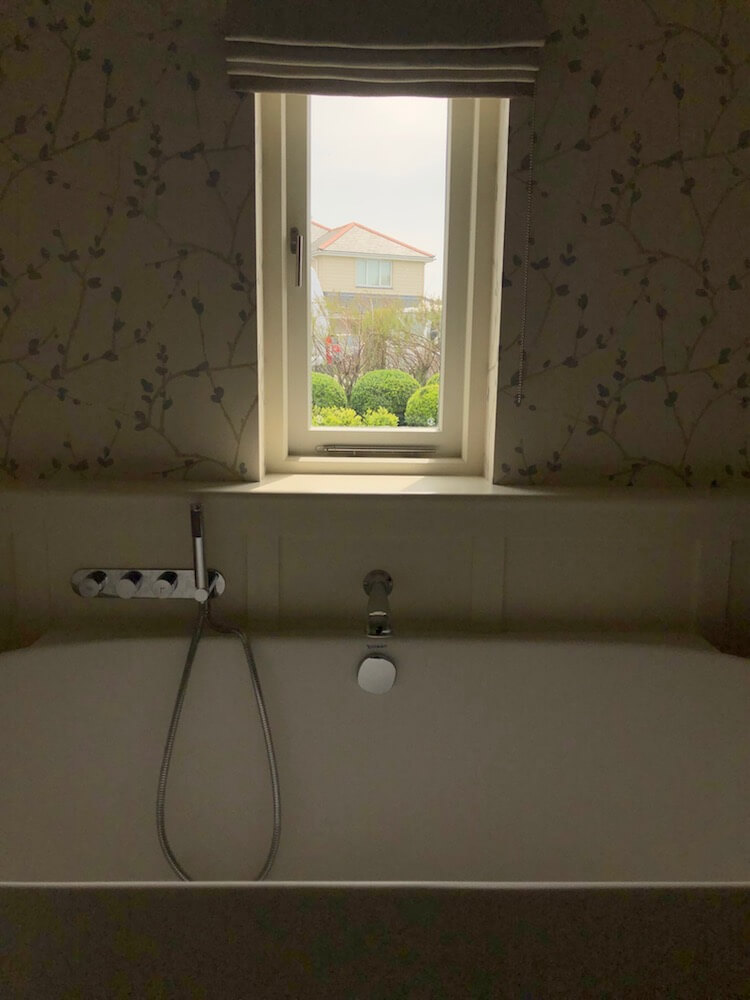 bathroom window with bath and wallpaper looking out at view of buxom balls