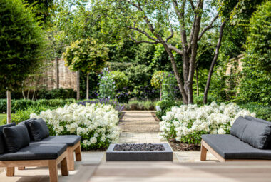 piet boon garden furniture in a townhouse garden in Oxford, with white Bobo Hydrangeas lining a path behind. The background is a faded productive garden with Sweet peas on metal obelisks