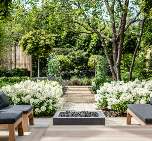 piet boon garden furniture in a townhouse garden in Oxford, with white Bobo Hydrangeas lining a path behind. The background is a faded productive garden with Sweet peas on metal obelisks