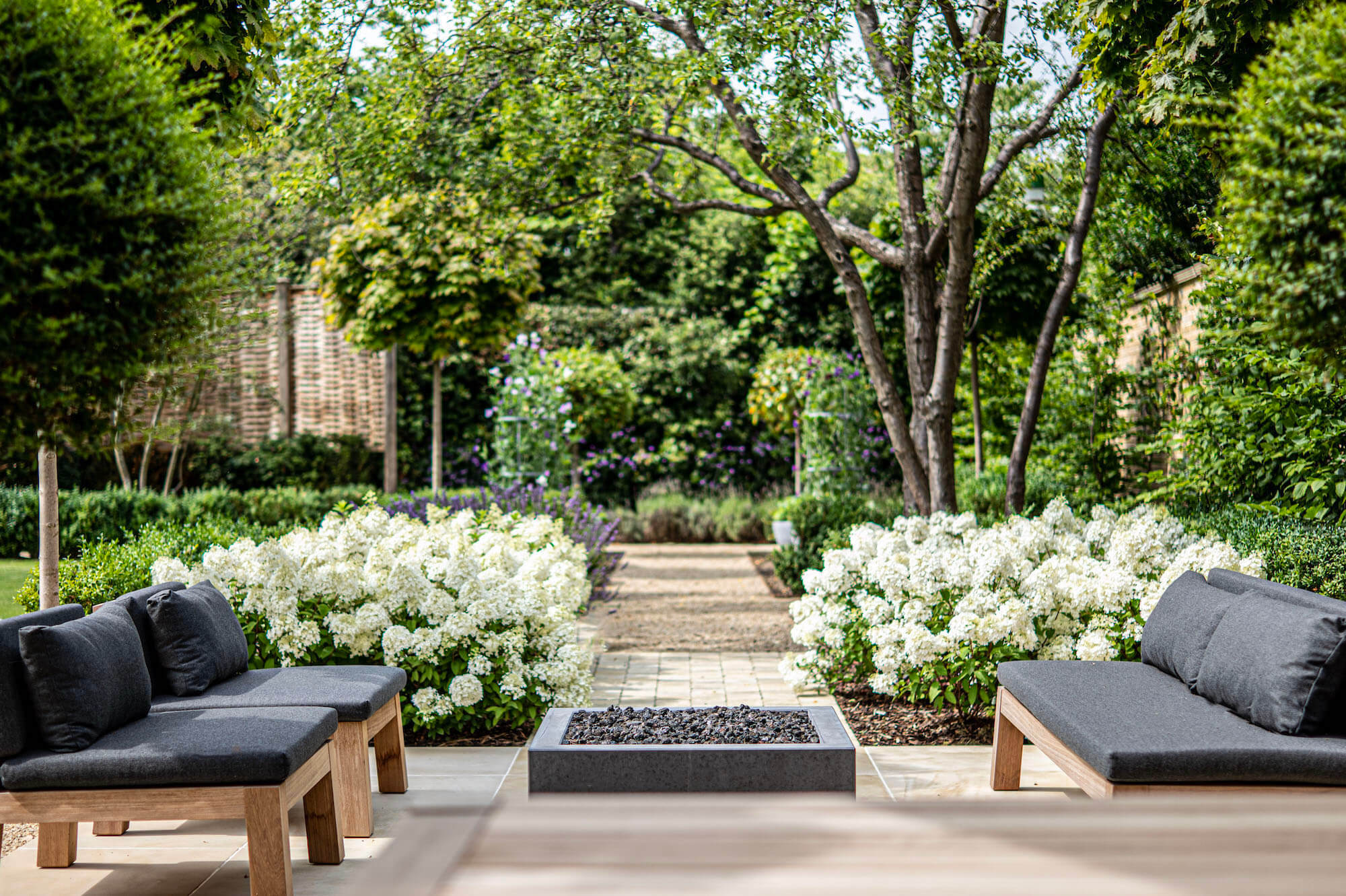 piet boon garden furniture in a townhouse garden in Oxford, with white Bobo Hydrangeas lining a path behind. The background is a faded productive garden with Sweet peas on metal obelisks
