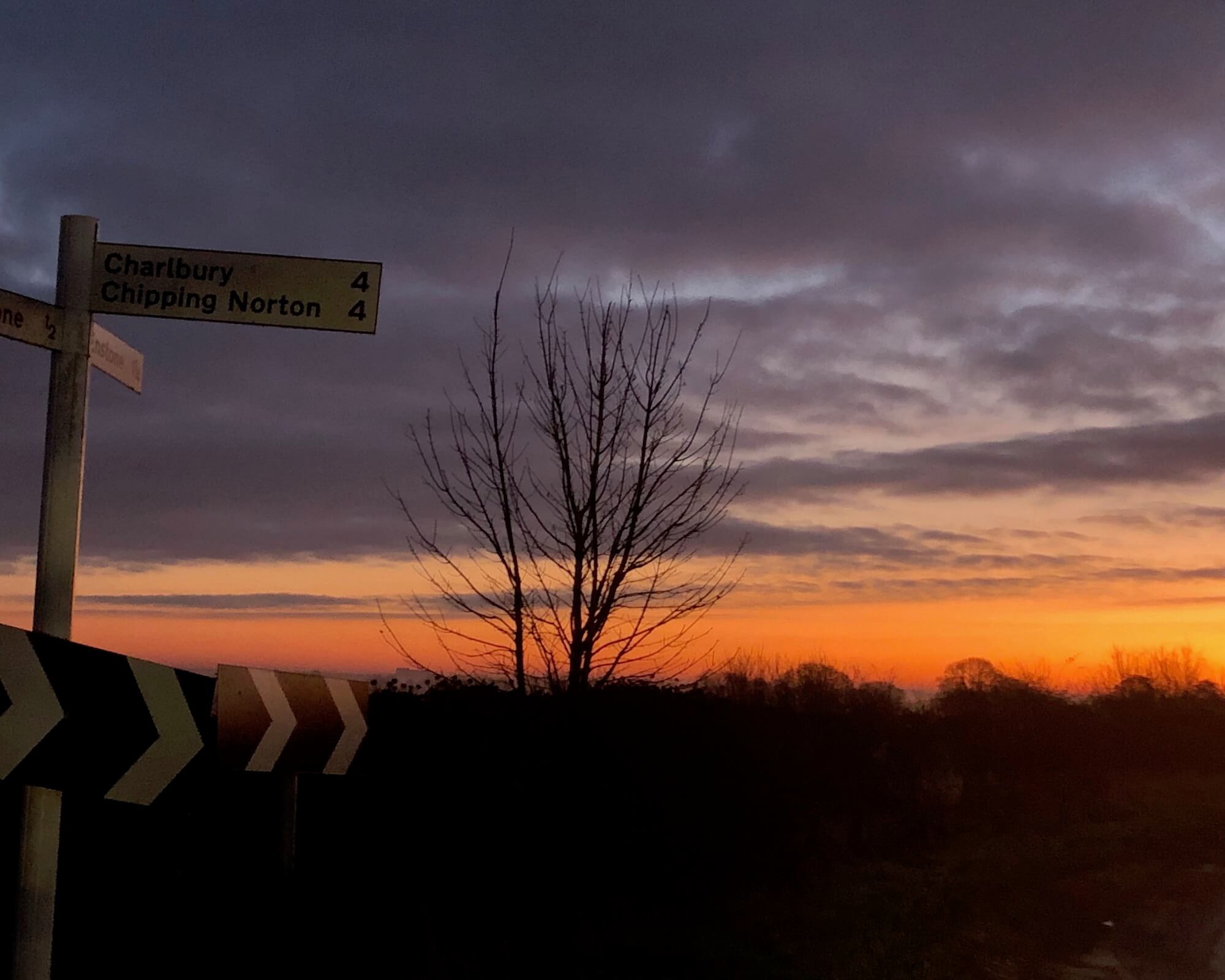 crossroads signs on a red dawn morning directing Charlbury and Chipping Norton 4 miles each