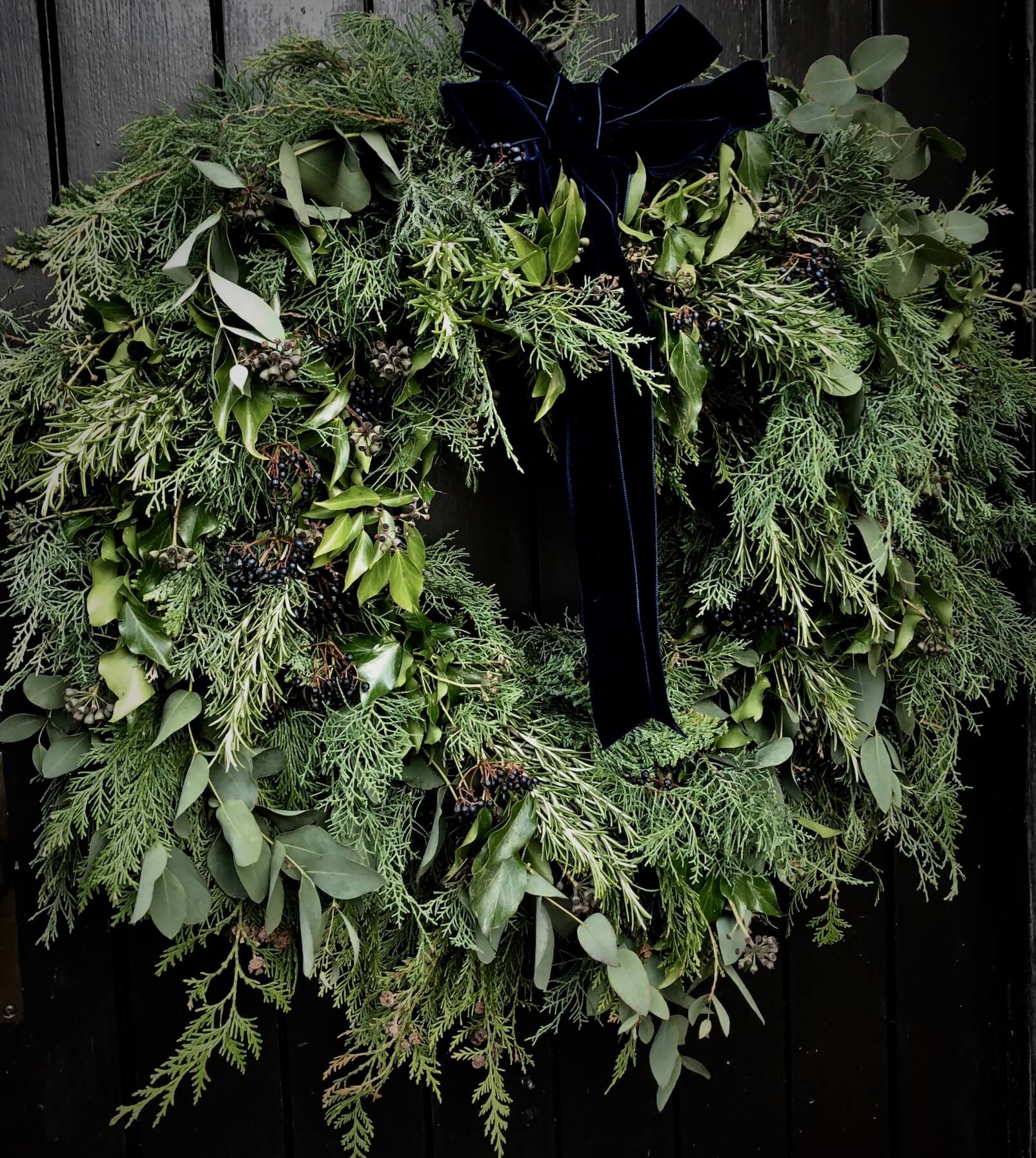 a foraged wreath in the Cotswolds England on a black door with a blue ribbon
