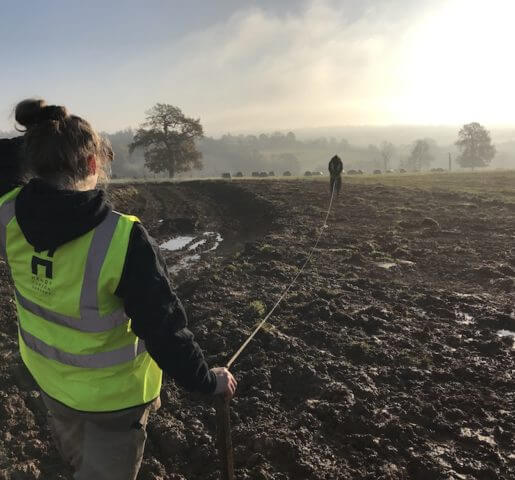 female landscaper in uniform measuring large muddy landscape site