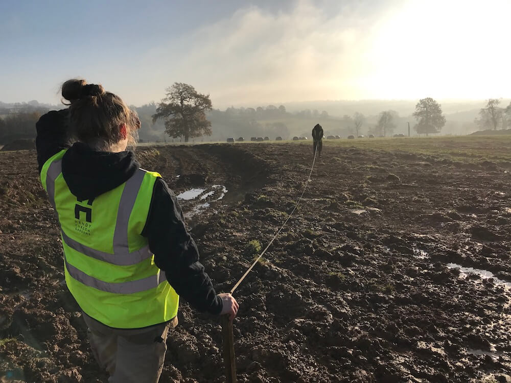 female landscaper in uniform measuring large muddy landscape site