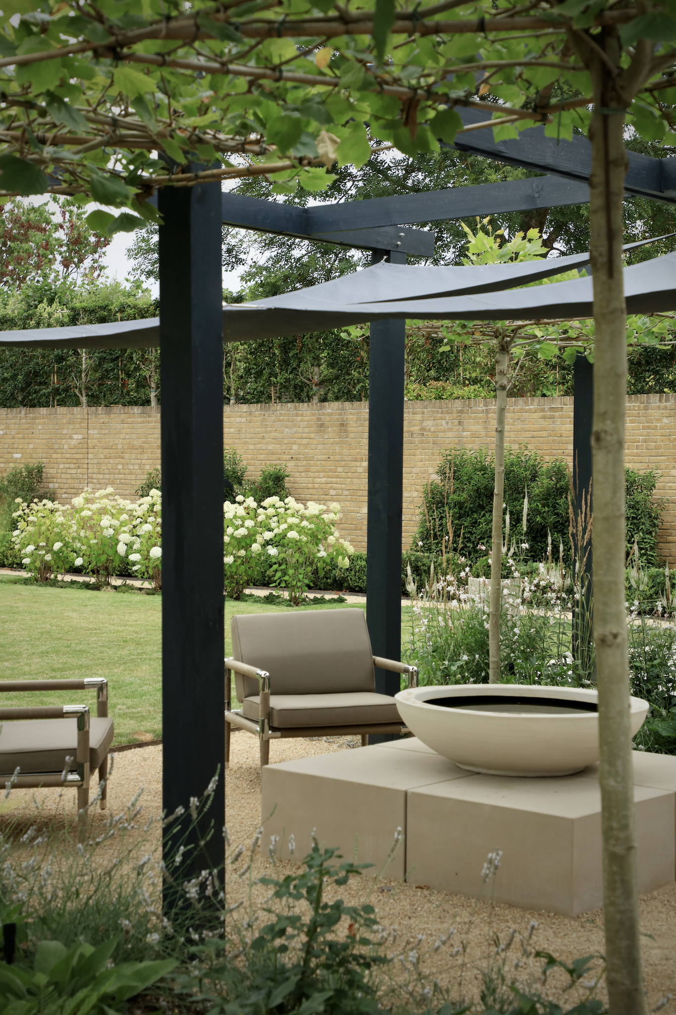 Pleached trees through the arbor looking on to realxed seating area with waterbowl and indian ocean furniture