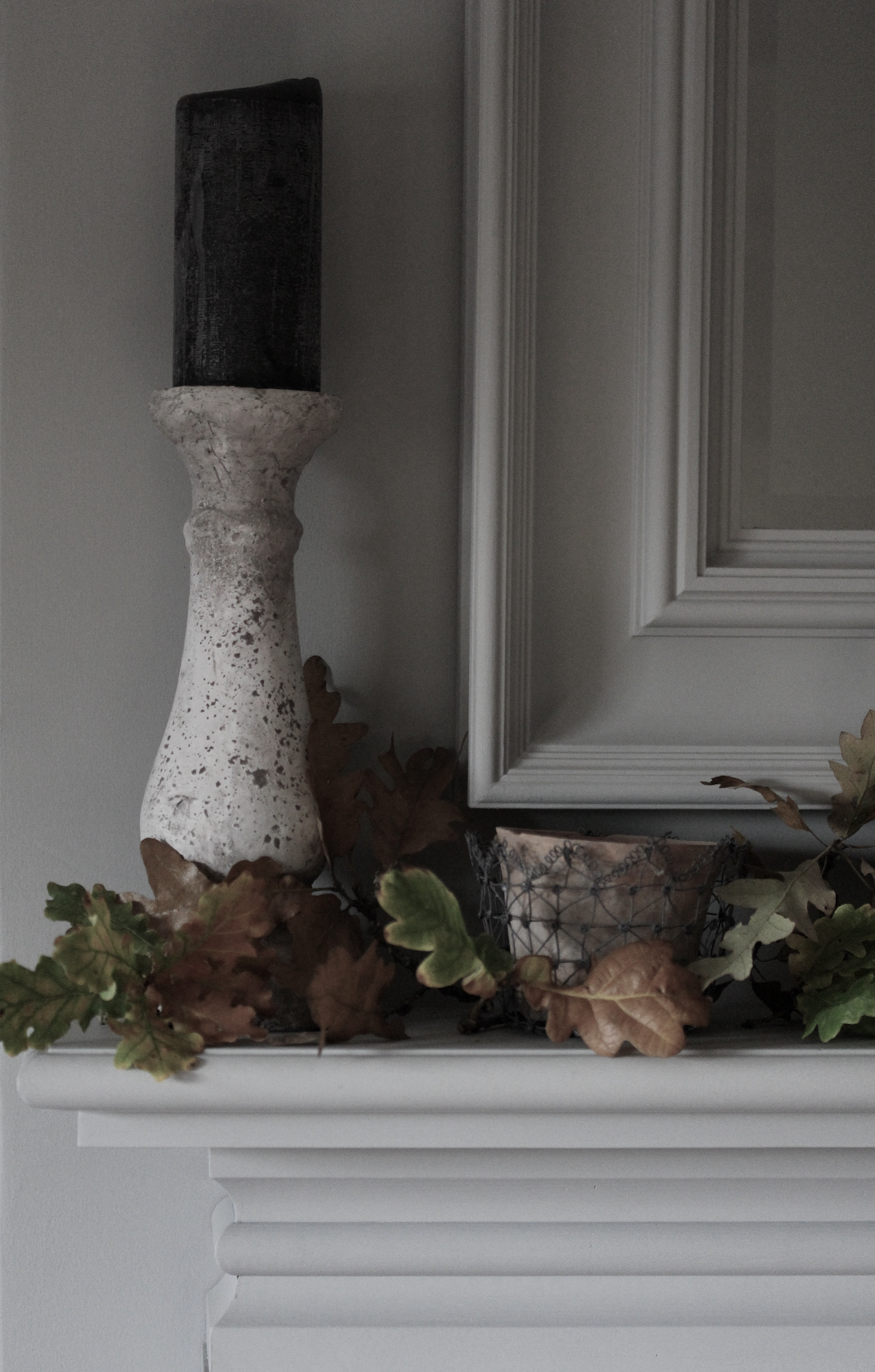 Candle on distressed pillar surrounded by Autumnal leaves on Oxford mantlepiece 