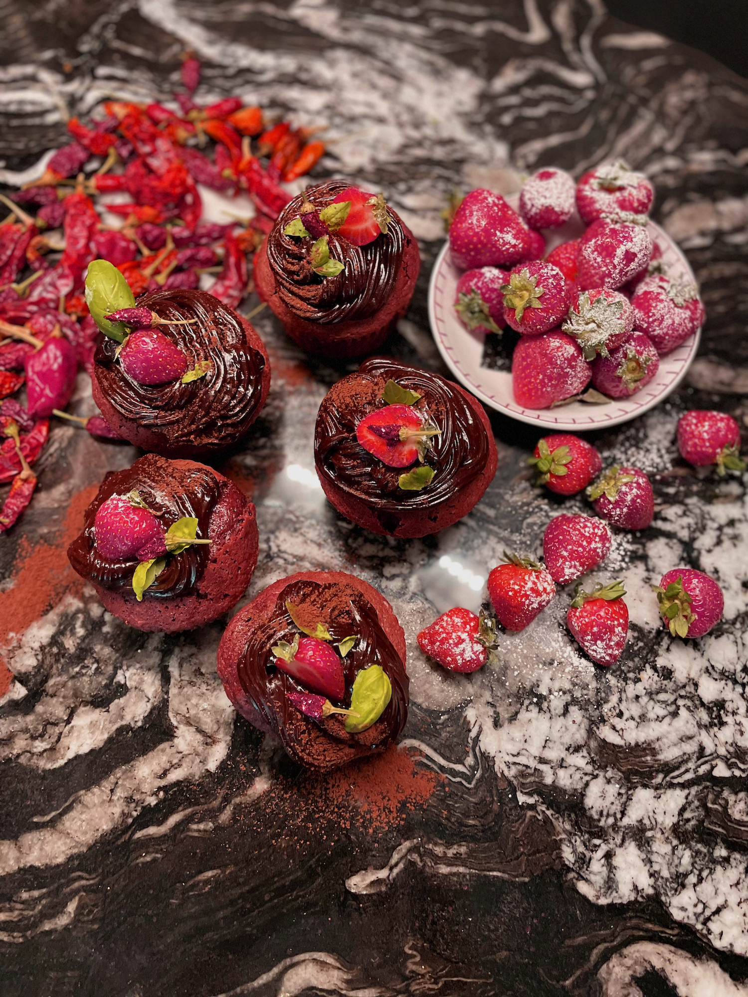 Rich red velvet strawberry, basil and chilli cupcakes on quartz worktop