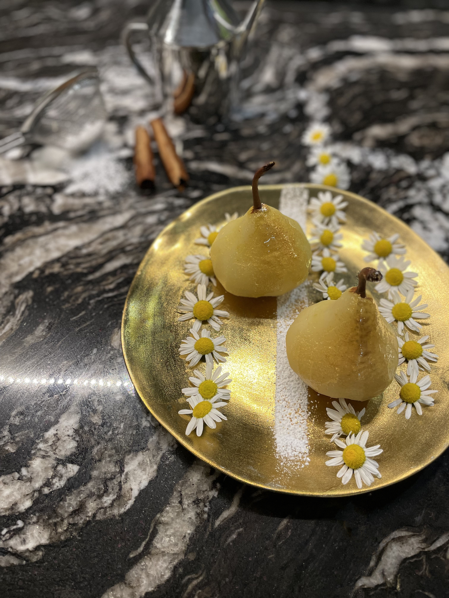 Spiced poached pears on black quartz worktop garnished with camomile and cinnamon 