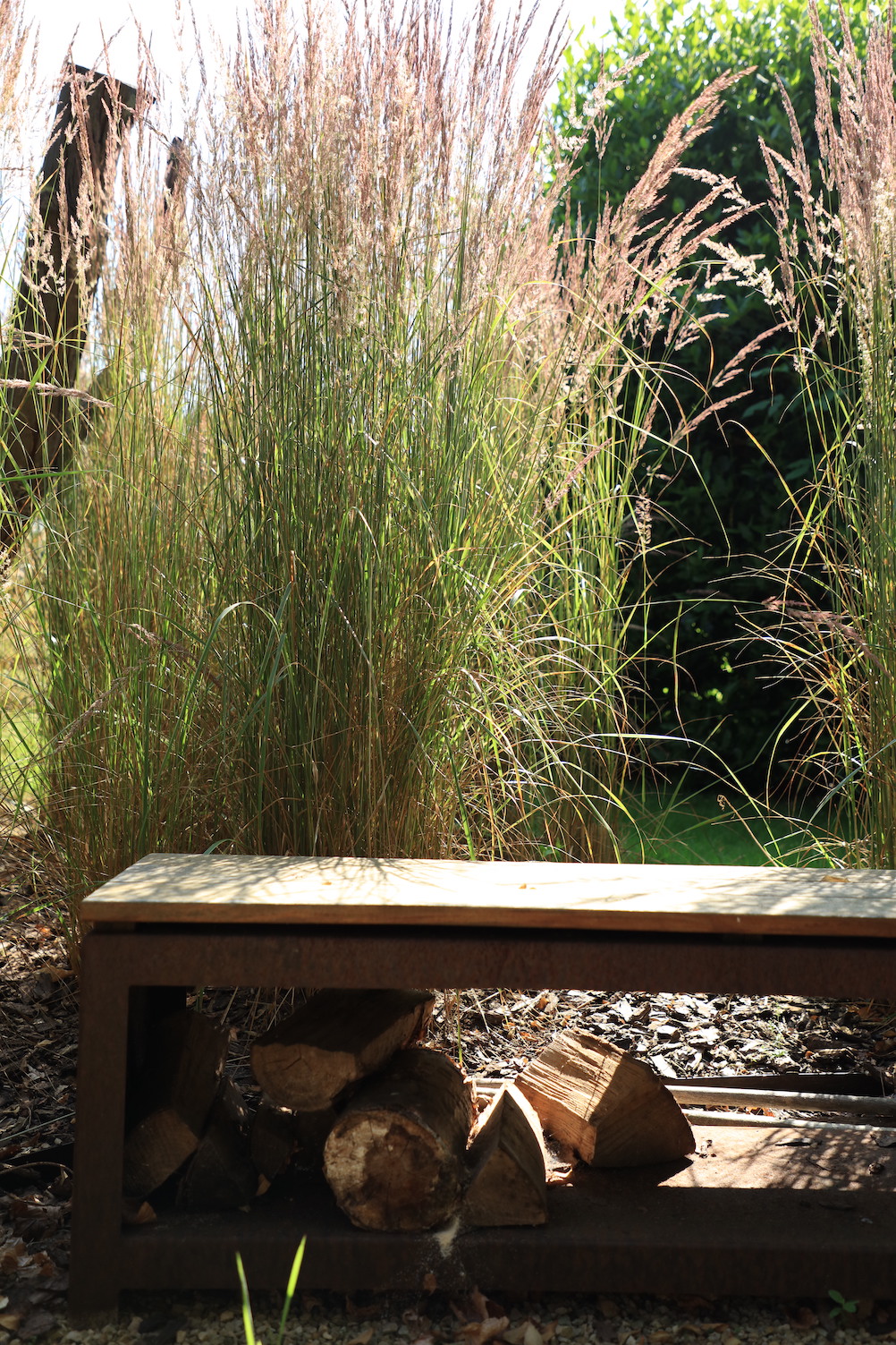 Wooden bench and log store in cotswold garden with grasses surrounded
